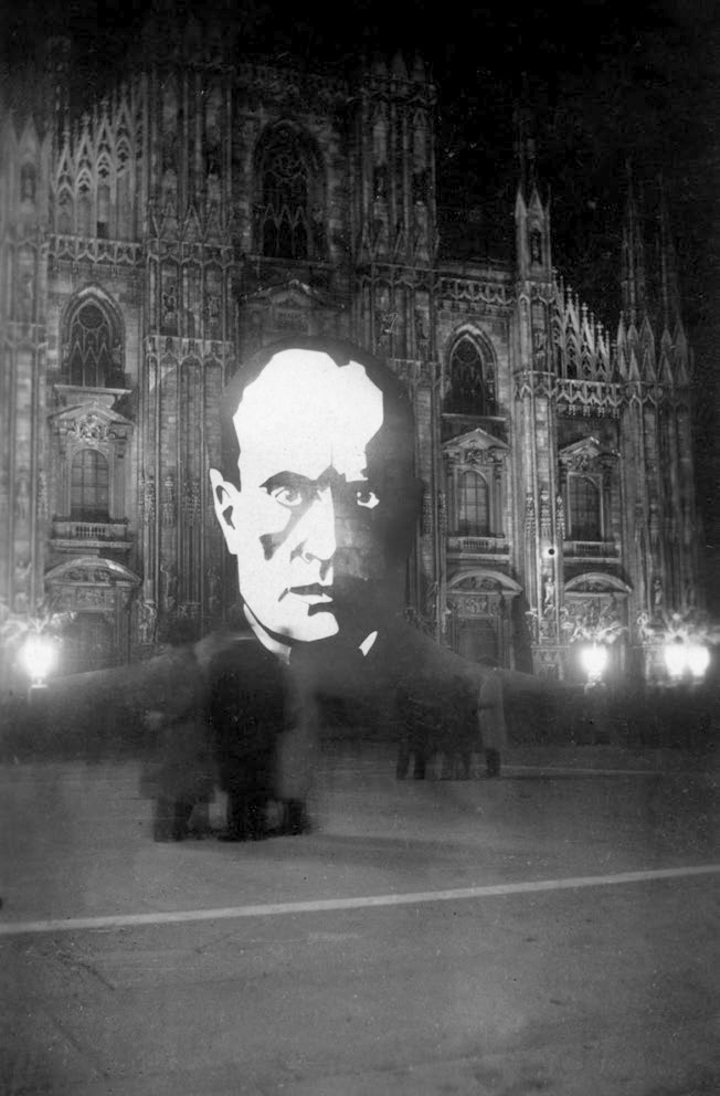 À noite, em frente ao Duomo de Milão, a imagem iluminada de Mussolini, que contou com o apoio do cardeal Schuster até novembro de 1938, quando condenou as Leis Raciais do Duce.